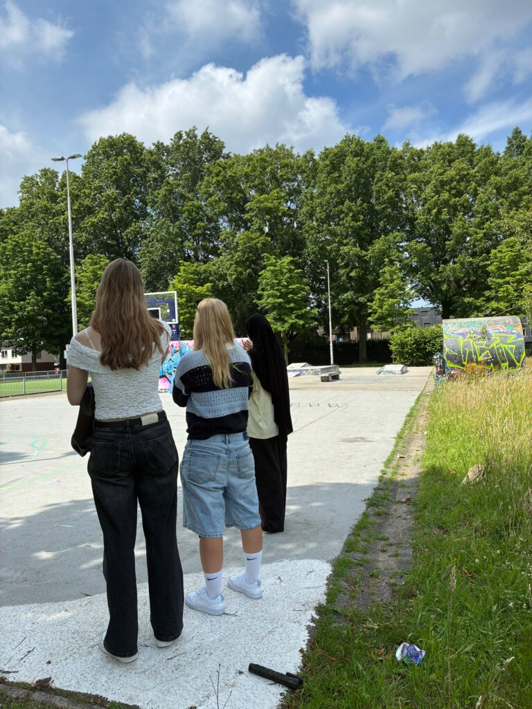 drie tienermeiden staan te kijken naar een stenen basketbalveld